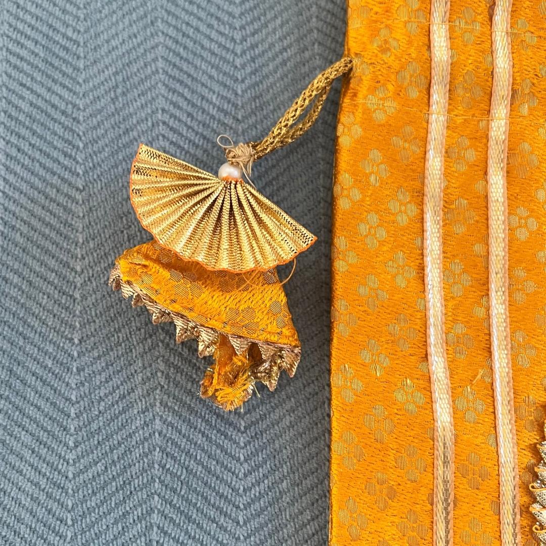 Gold fan-shaped pendant on a textured orange fabric background