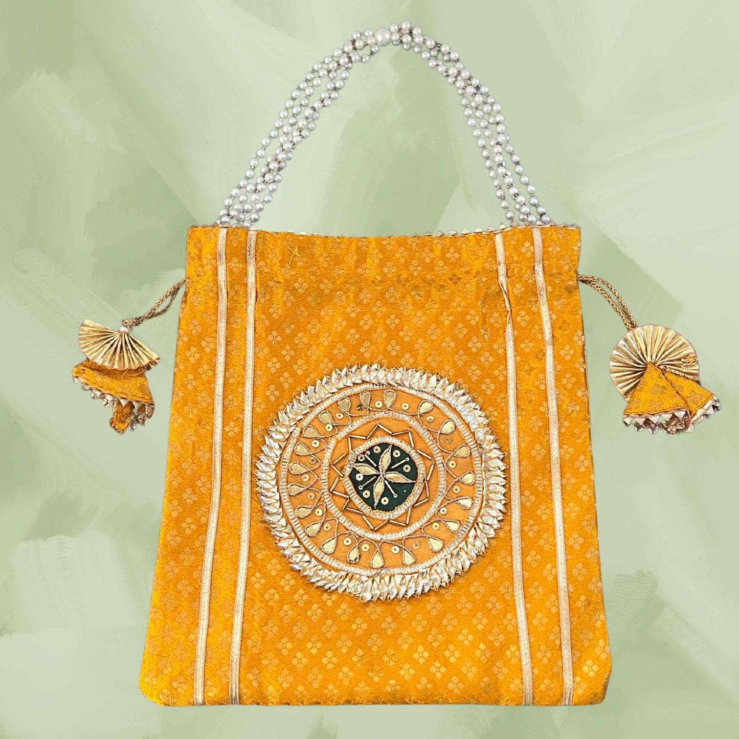 Decorative orange bag with intricate design and tassels on a light green background