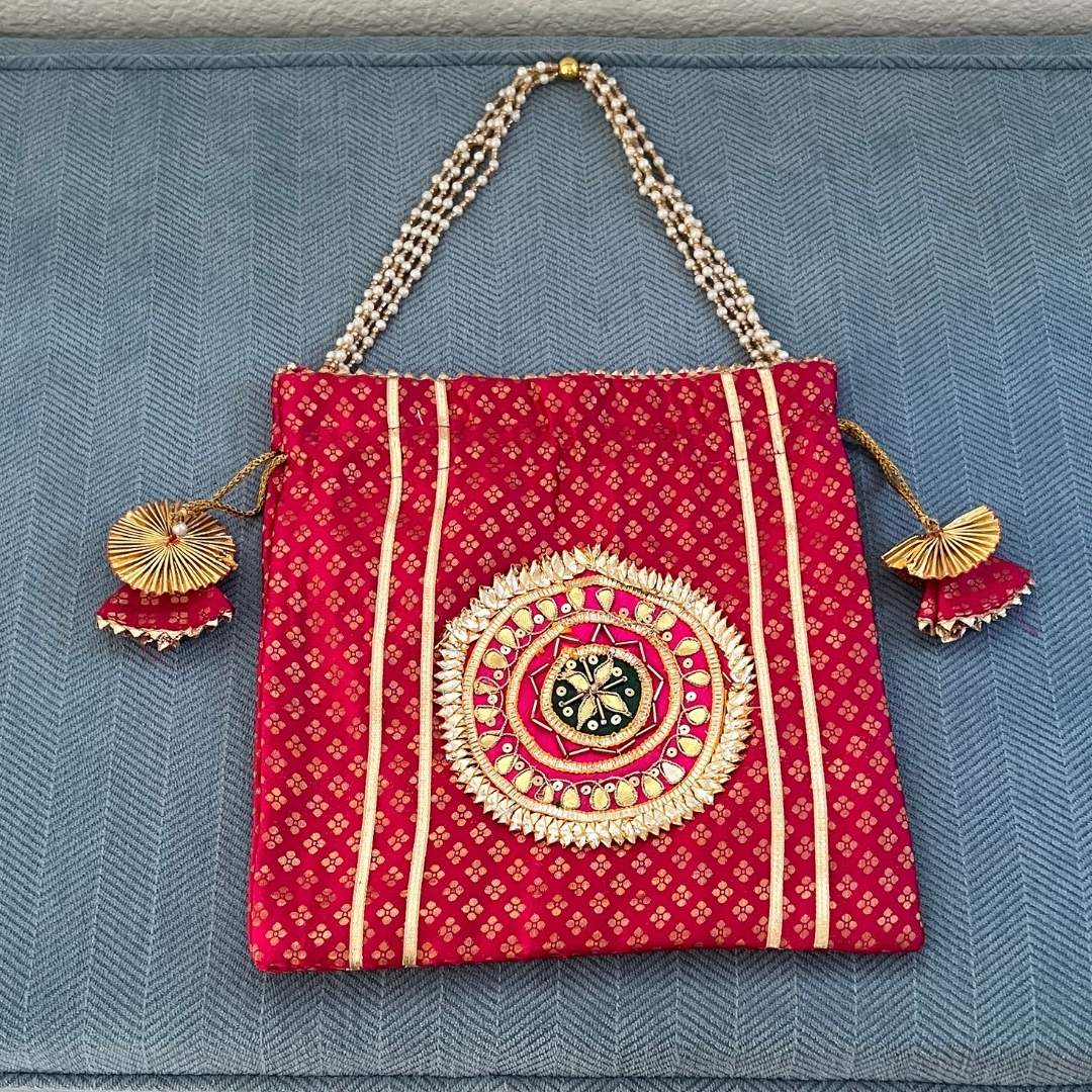 Decorative red bag with gold patterns and tassels on a blue textured background
