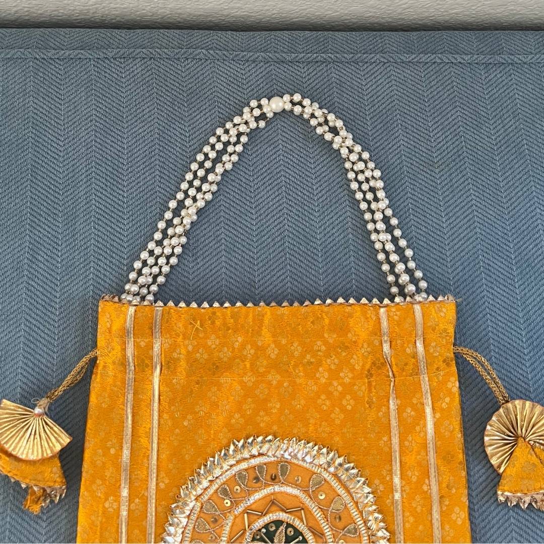 Decorative yellow bag with intricate designs and pearl handle on a textured blue background