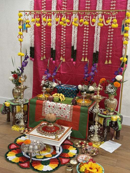 Pink fabric backdrop hung with vertical white jasmine garlands and marigold danglers behind a decorated chowki