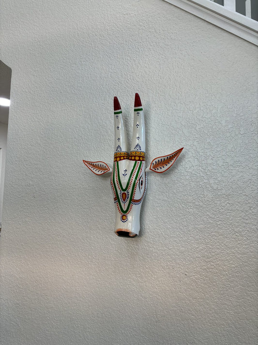 Hand-carved wooden Nandi head wall art in white with red and gold painted horns, mounted on a plain interior wall