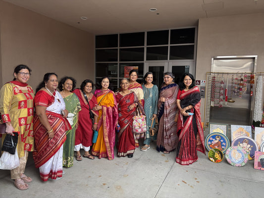 Urli Utsav Decor team and customers in festive sarees beside the Urli Utsav booth at a Bay Area Diwali mela, with hanging torans and hand-painted wall plates on display.