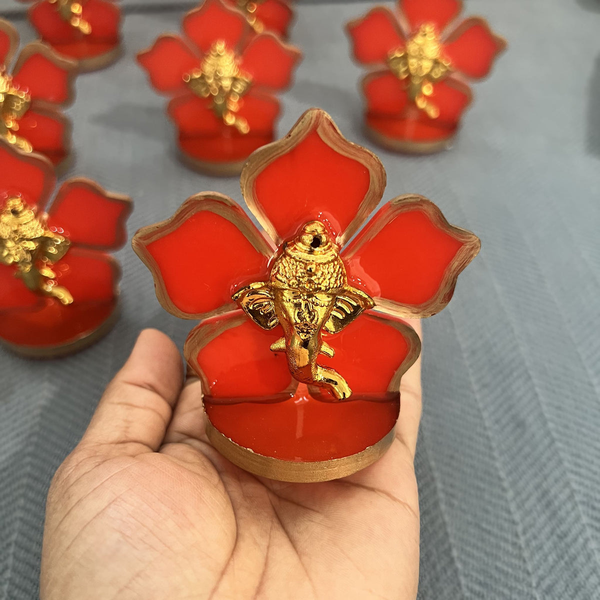Red flower Ganesha car idol with gold Ganesha face held in a palm to show its 3 inch size