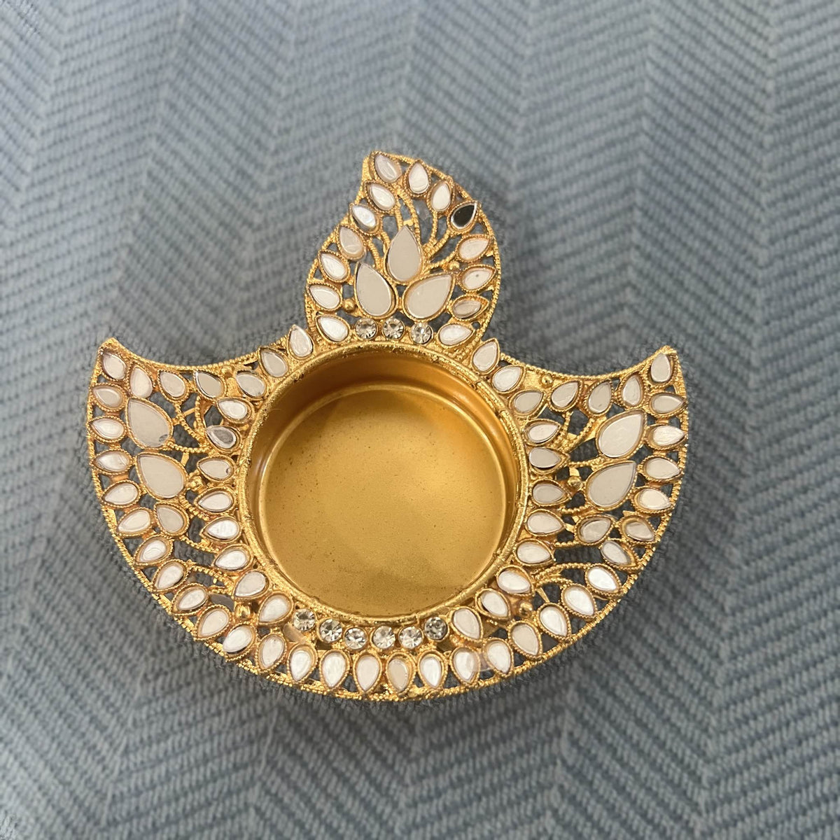 Close-up of a gold mirror deep (flame-shaped diya) tea light holder on a blue herringbone cloth