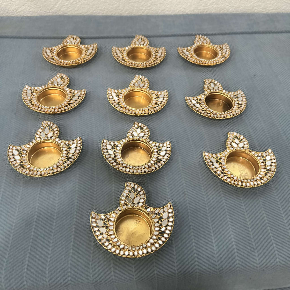 Set of ten flame-shaped gold mirror diya tea light holders, seen from an angle on blue fabric
