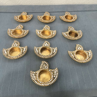 Set of ten flame-shaped gold mirror diya tea light holders, seen from an angle on blue fabric