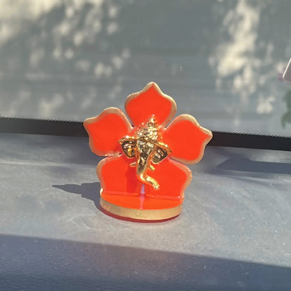 Close-up of a gold Ganesha car idol on a red five-petal flower base on a dashboard
