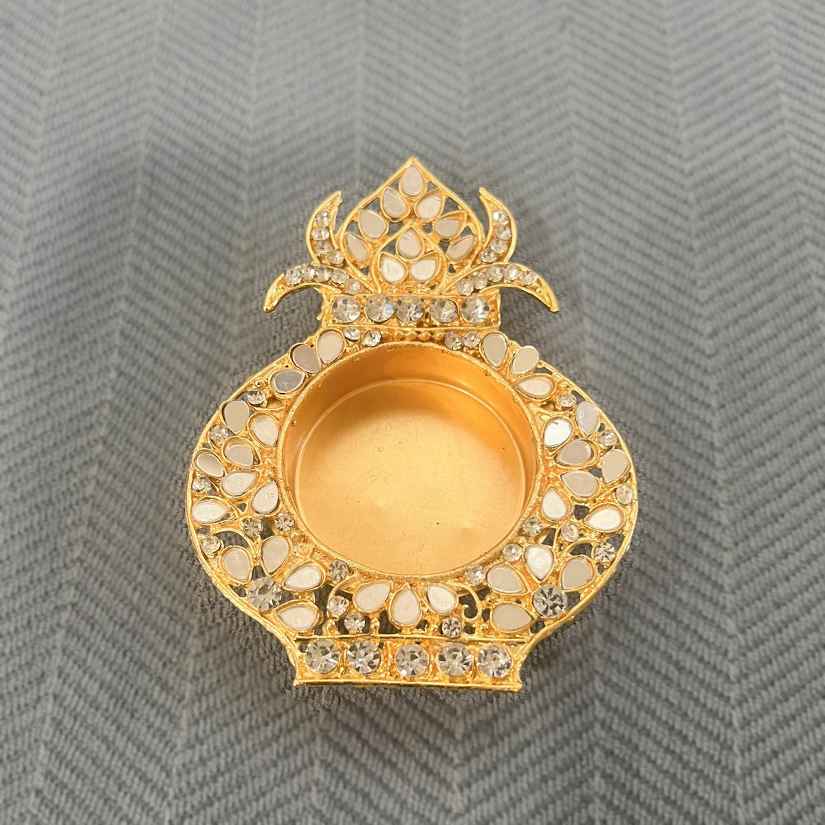 Single gold kalash-shaped tea light holder set with white mirrors, on a blue herringbone cloth