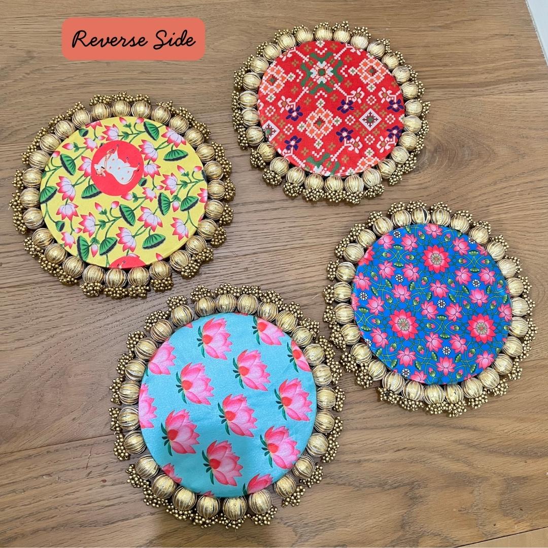 Reverse faces of the four Patola brocade mats: yellow floral, red geometric, blue with pink flowers and pale blue rose, each rimmed with gold beads.