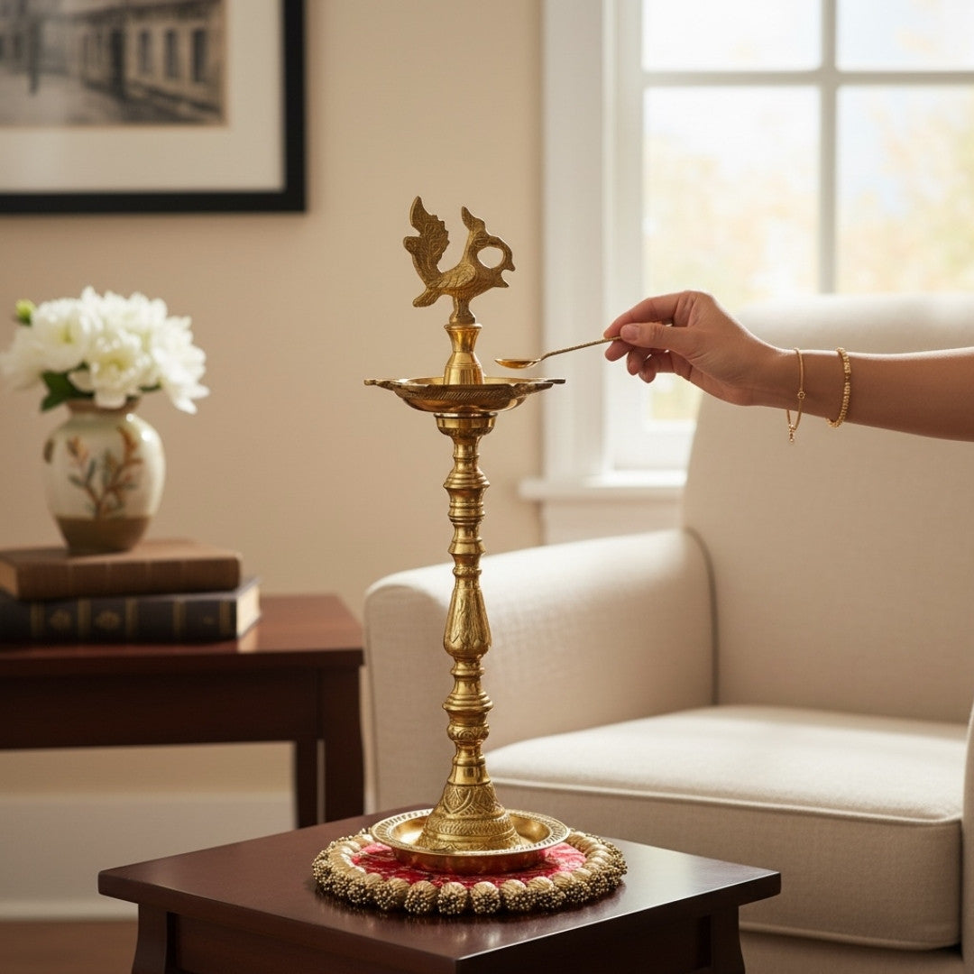 Tall brass oil lamp on a pink Patola brocade mat with a gold beaded border, a hand reaching in to light the wick.