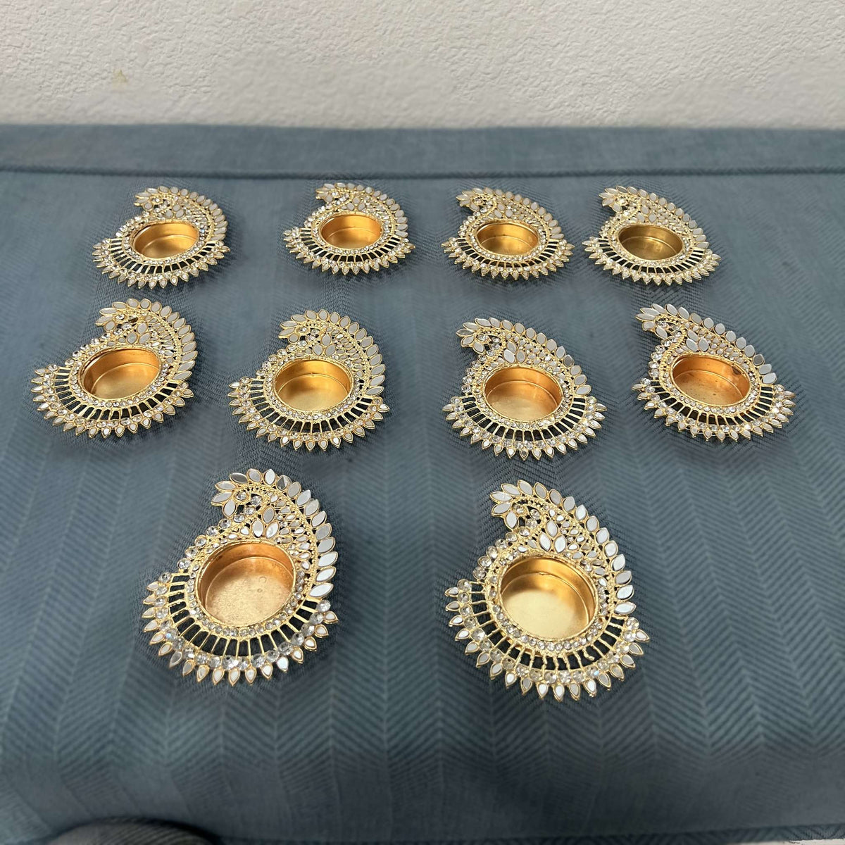 Ten mango paisley mirror tea light holders on a blue cloth, seen from an angle