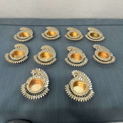 Ten mango paisley mirror tea light holders on a blue cloth, seen from an angle