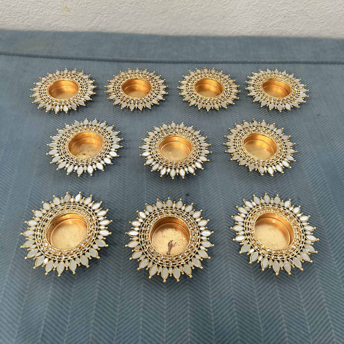 Ten gold mirror sunflower tea light holders in rows on a blue herringbone cloth