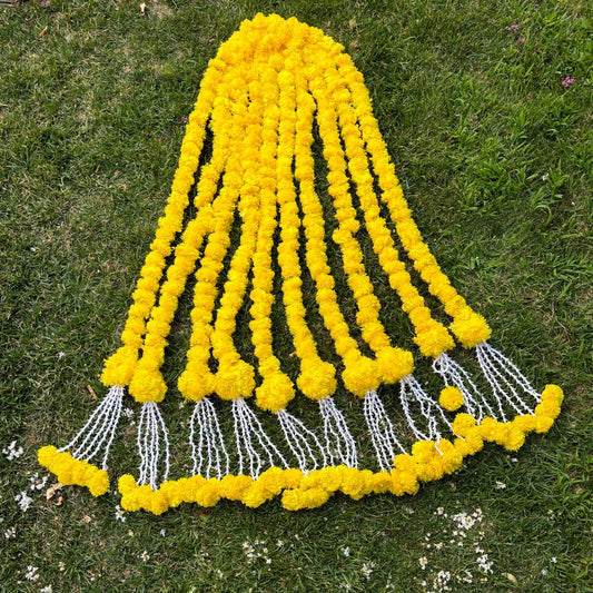 Ten yellow marigold ball garland strings with white tassel ends laid on grass