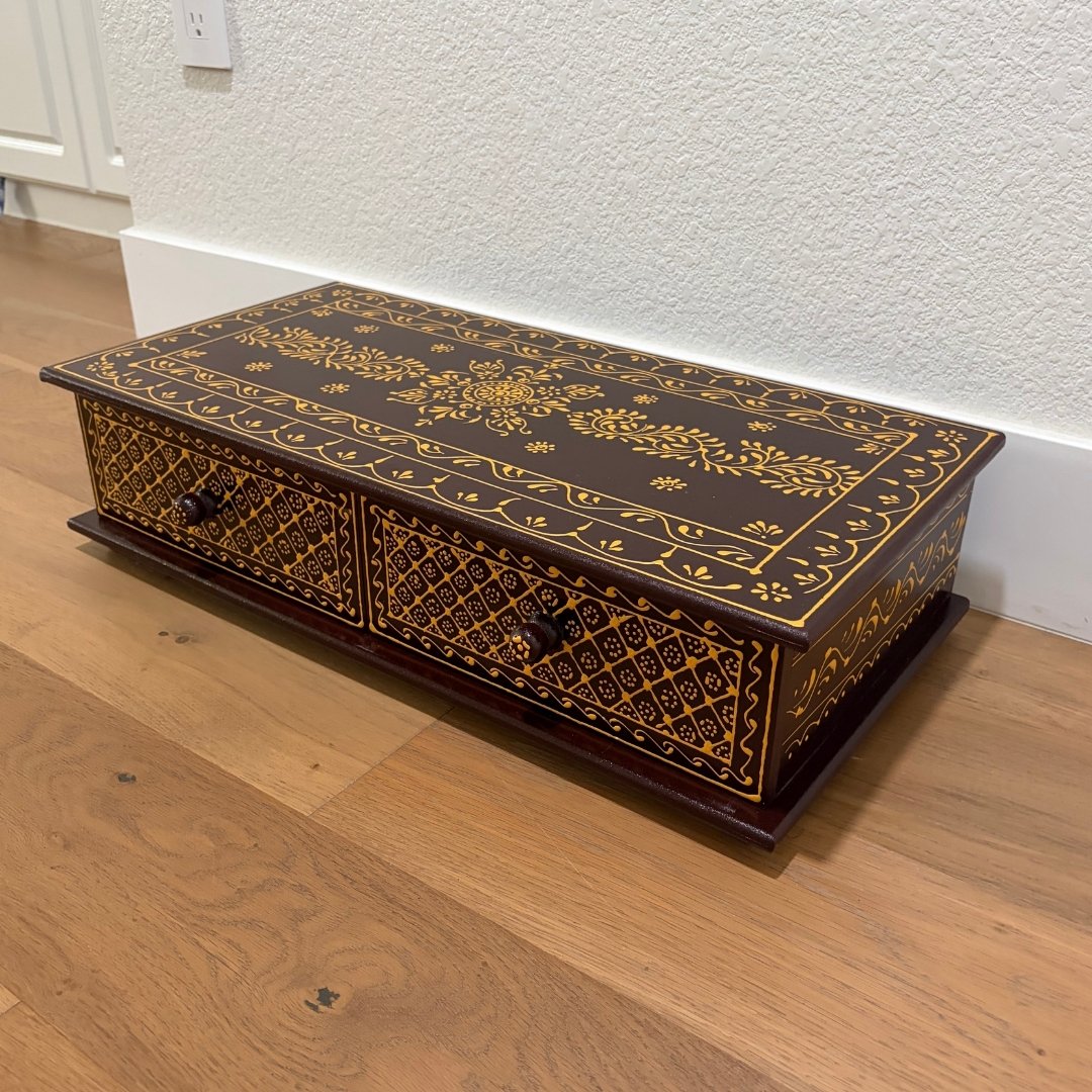 Decorative wooden box with intricate gold patterns on a wooden floor.