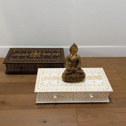 Decorative box with intricate patterns and a small Buddha statue on a wooden surface.