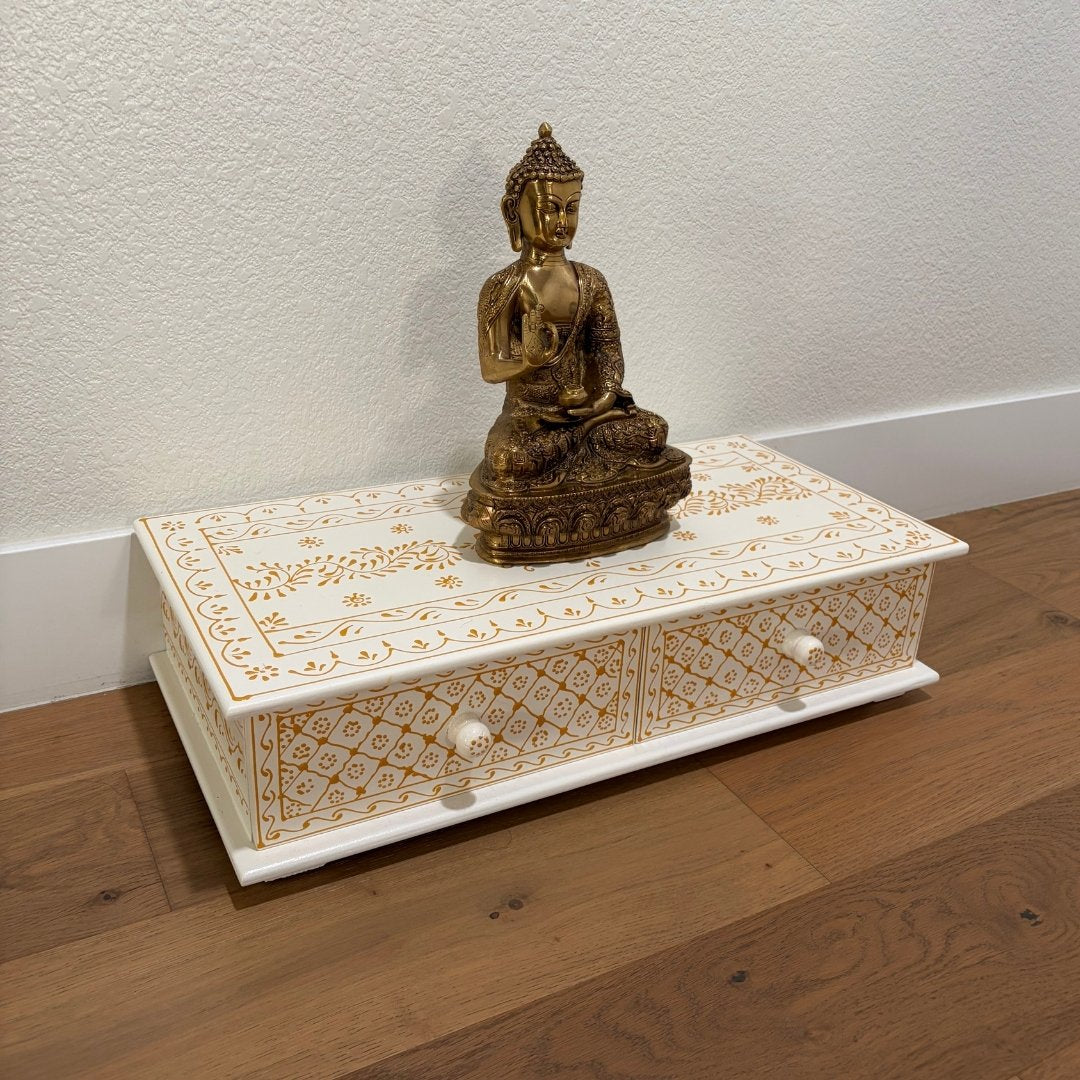 Decorative wooden box with intricate carvings and a gold Buddha statue on a wooden floor.