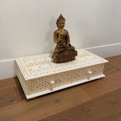 Decorative wooden box with intricate carvings and a gold Buddha statue on a wooden floor.