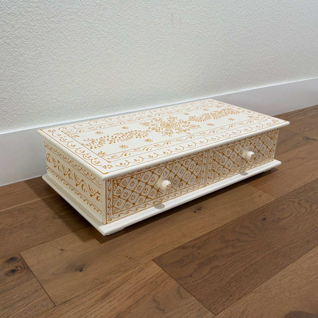 Decorative wooden box with intricate gold patterns on a wooden floor.