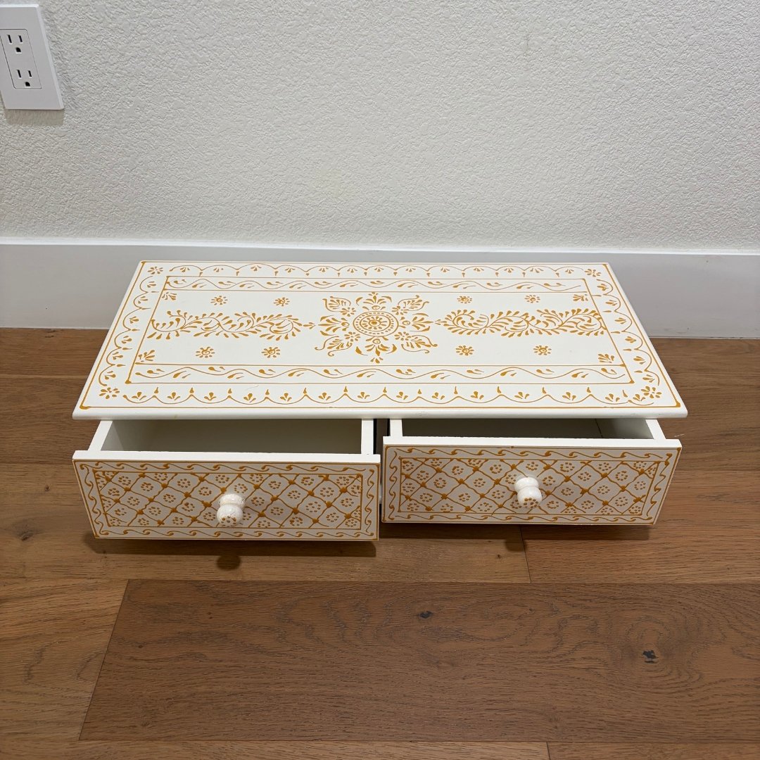 Decorative wooden box with intricate gold patterns on a wooden floor.
