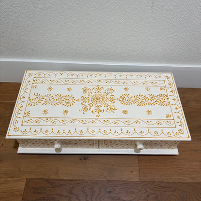 Decorative white box with gold intricate patterns on a wooden floor.