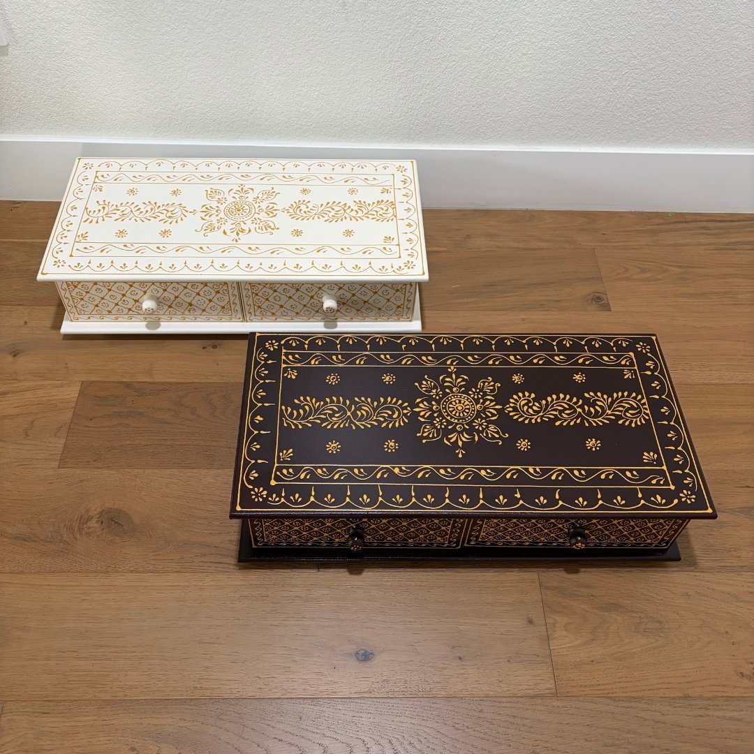 Two ornate boxes, one white and one black with gold patterns, on a wooden floor.