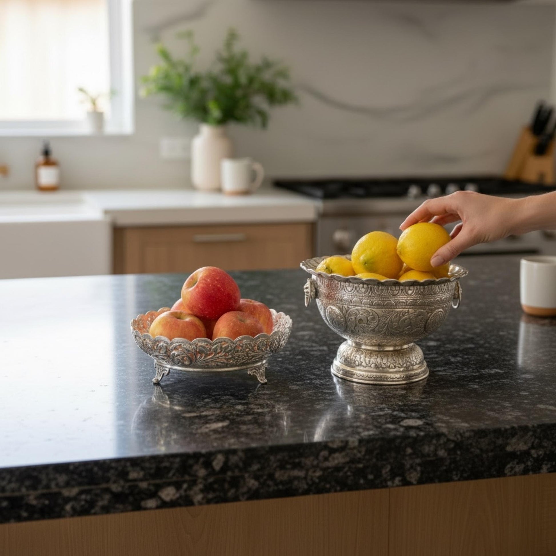 German silver fruit bowl with apples and lemons on kitchen counter with hand reaching