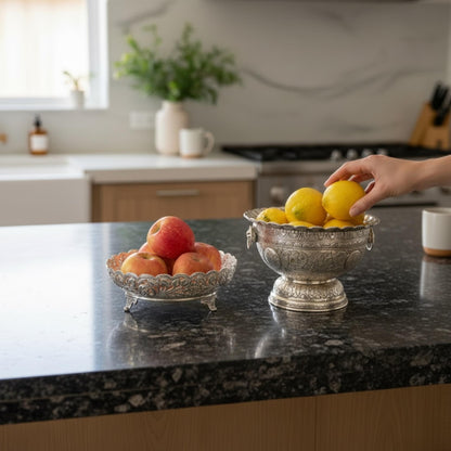 German silver fruit bowl with apples and lemons on kitchen counter with hand reaching