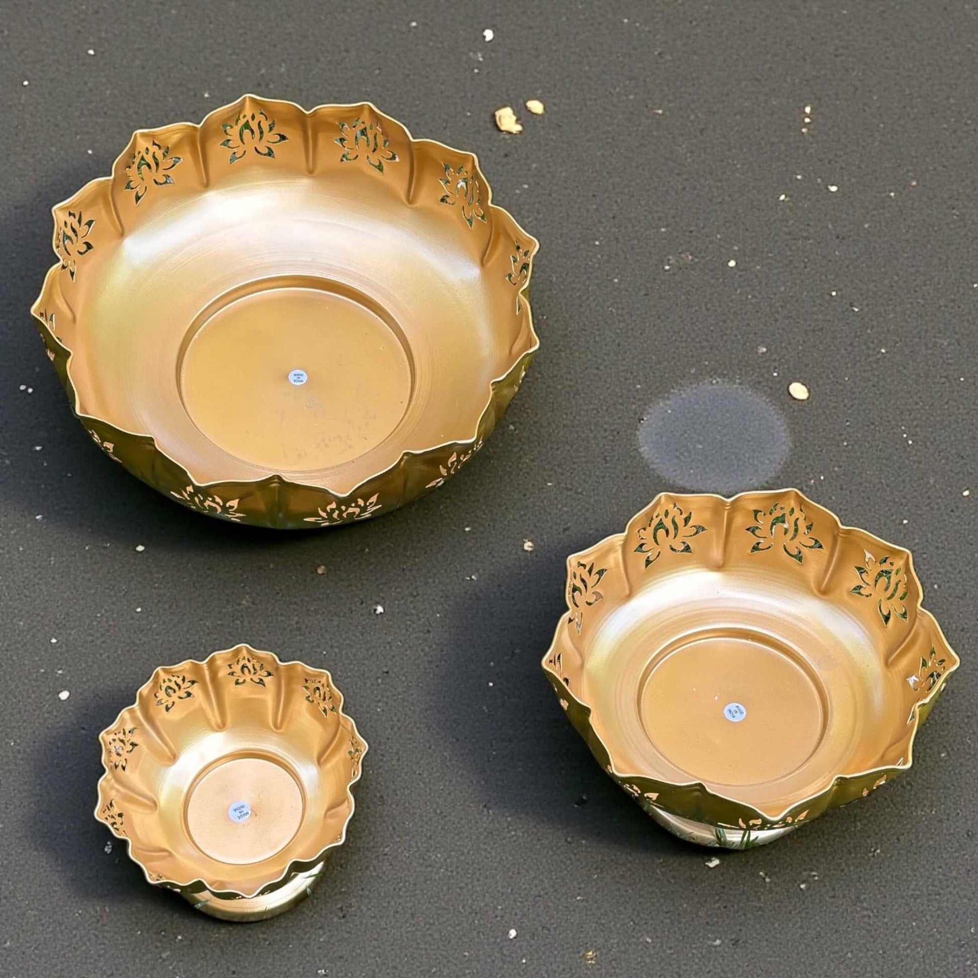 Overhead shot of the three urli bowls grouped on green grass, empty, showing their varied sizes and the textured lotus‑petal rims in a festive outdoor setting
