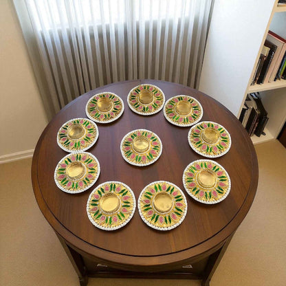 Ten pearl-rim floral diya holders arranged in a circle on round wooden table near window — handcrafted Diwali decor.