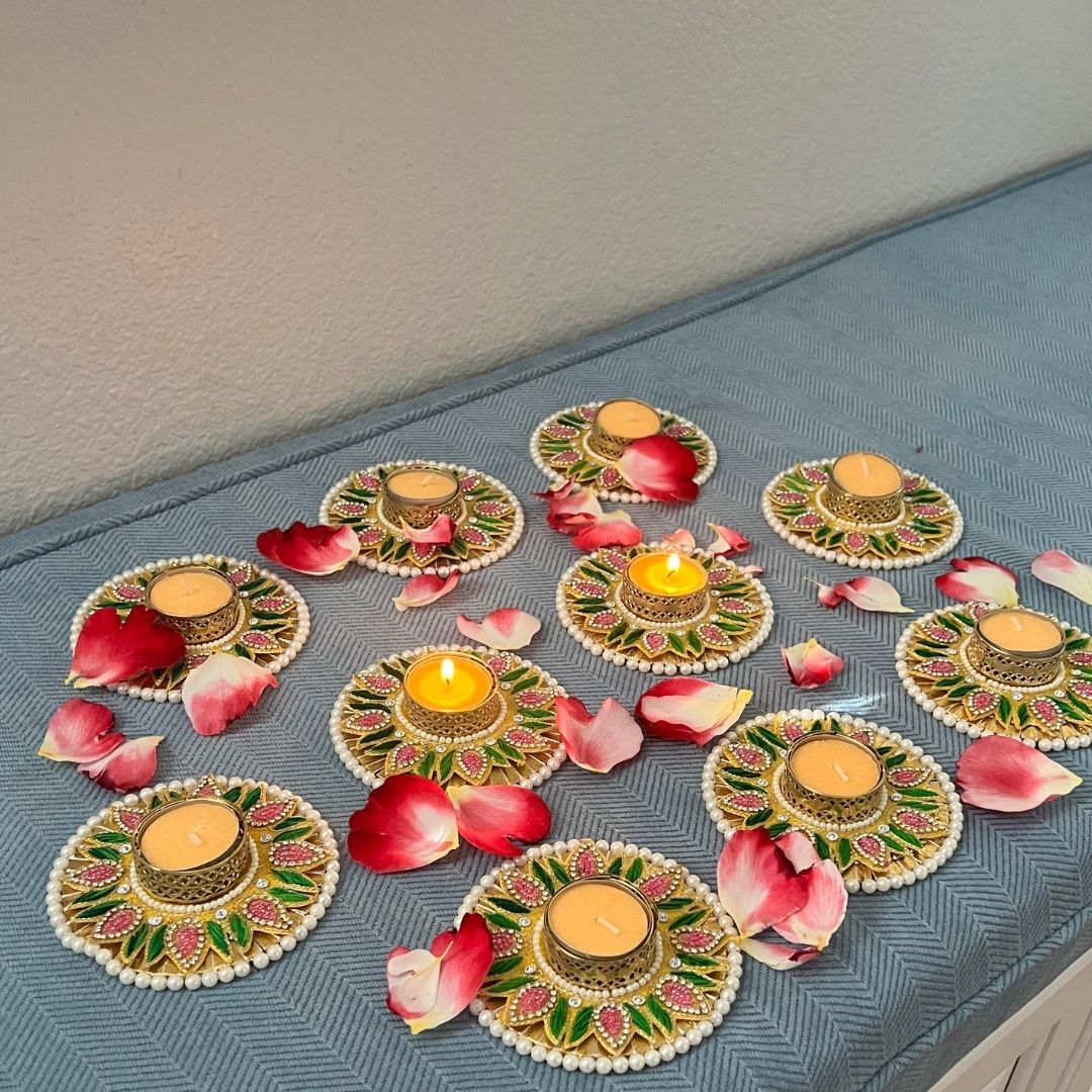 Decorative Diwali tea light holders with rose petals; pearl-edged pink and green floral diyas, some lit — wedding/pooja decor.