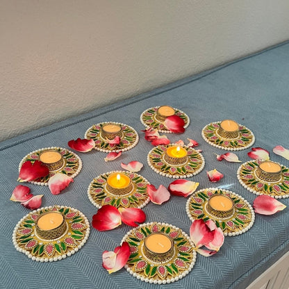 Decorative Diwali tea light holders with rose petals; pearl-edged pink and green floral diyas, some lit — wedding/pooja decor.