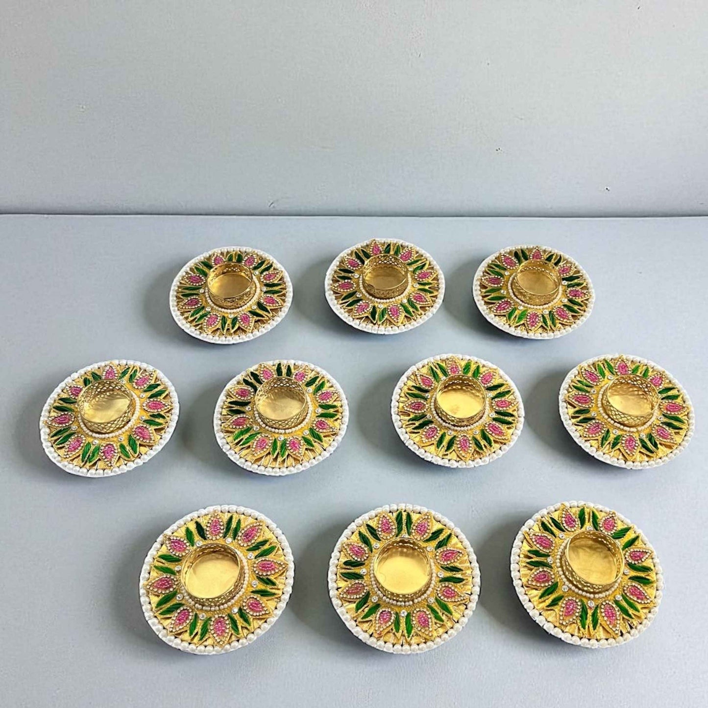 Complete set of 10 decorative T-light holders on neutral backdrop; gold, pink and green floral design with pearl edging.