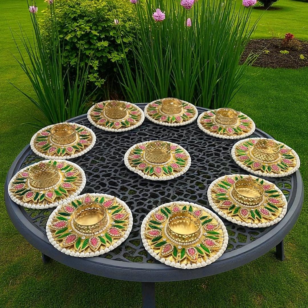 Ten multicolor Diwali tea light holders displayed outdoors on black garden table with greenery — Urli Utsav festive set.