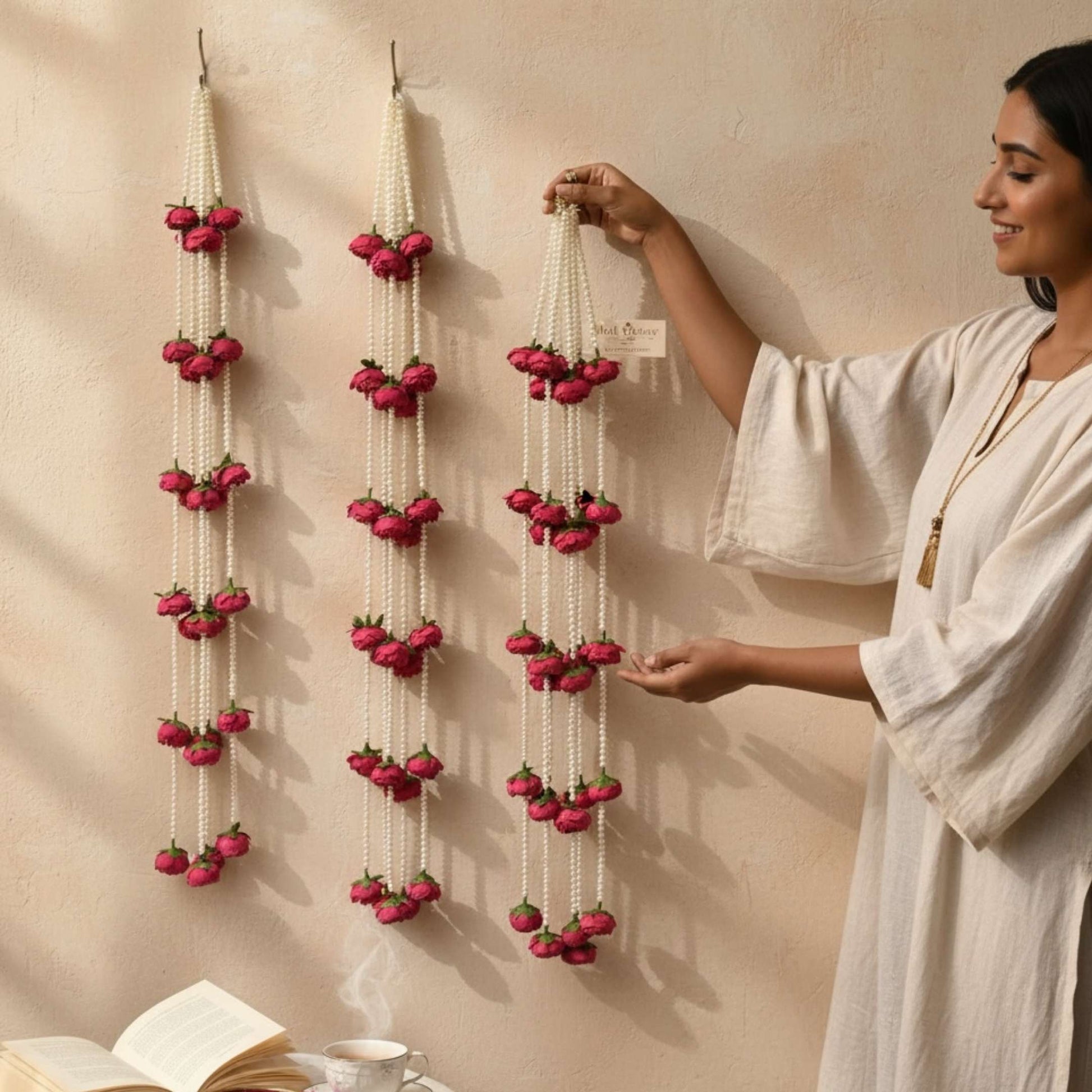 Woman arranging decorative 3FT red peony garlands with red flowers on a beige wall.