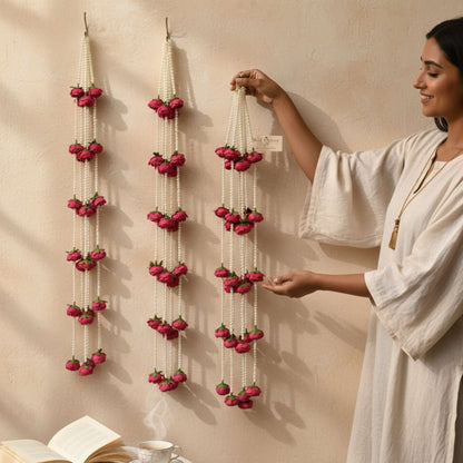 Woman arranging decorative 3FT red peony garlands with red flowers on a beige wall.