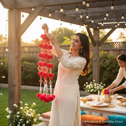 Woman decorating outdoor setting with red hanging decorations, surrounded by a garden and table with food.