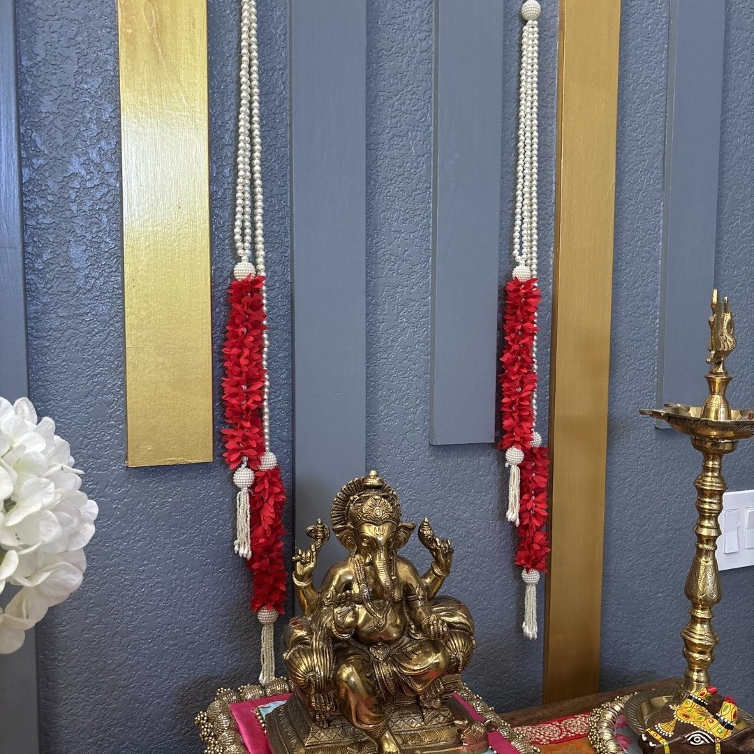 A golden Lord Ganesha idol placed on a decorated altar against a blue paneled wall with red floral garlands and gold vertical accents.