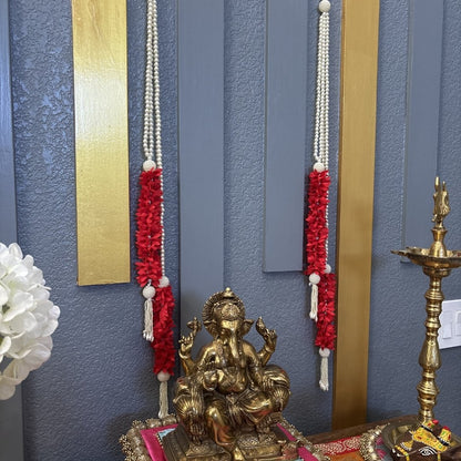 A golden Lord Ganesha idol placed on a decorated altar against a blue paneled wall with red floral garlands and gold vertical accents.