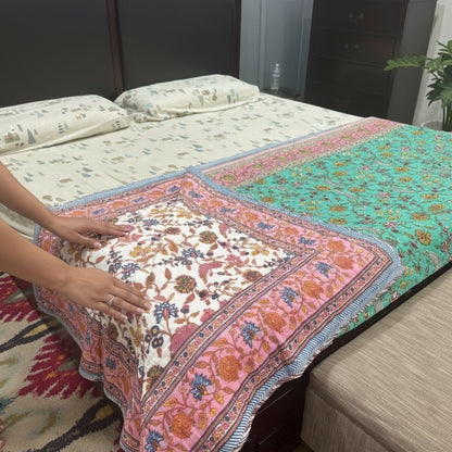 Person arranging a colorful floral-patterned bedspread on a bed.