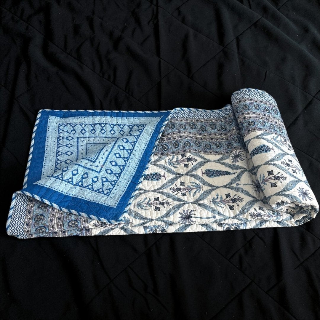 Rolled-up quilt with blue and white pattern on a black background