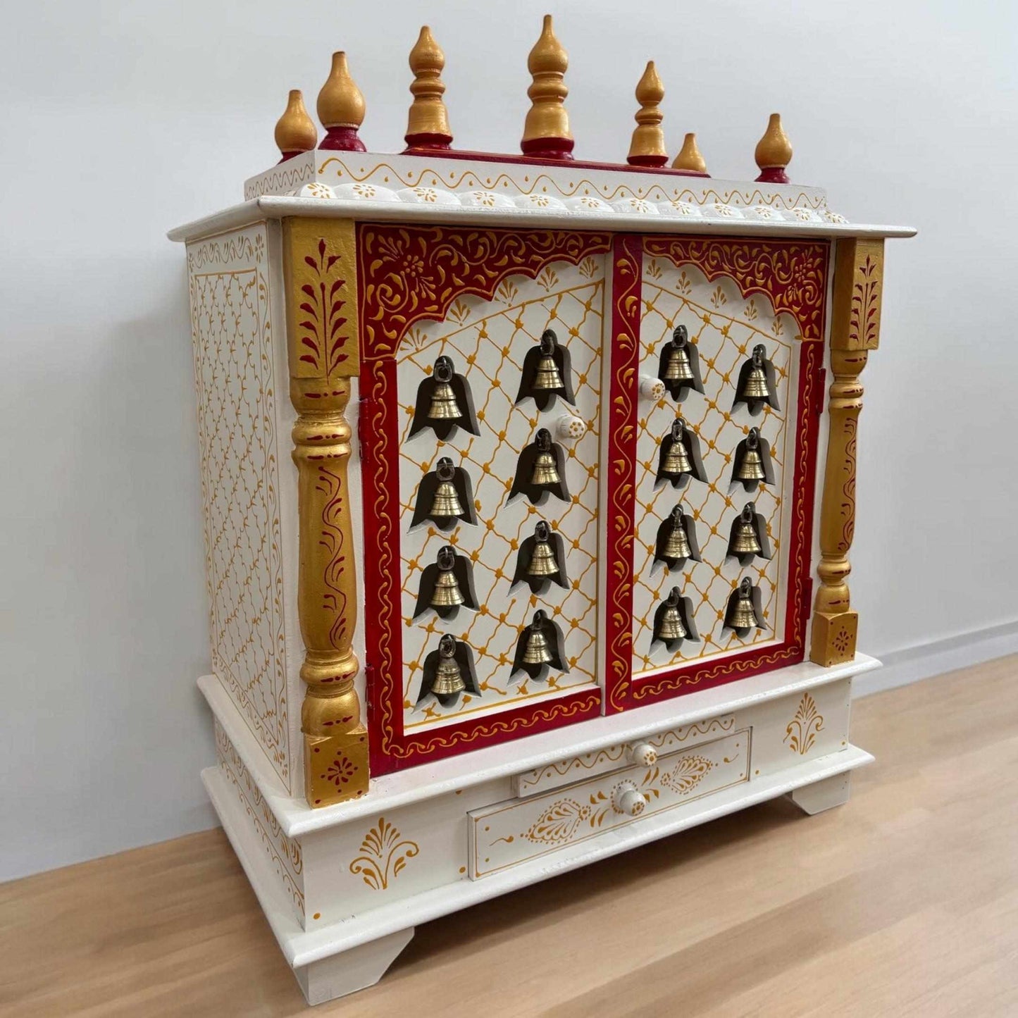 Decorative white and gold pooja mandir with bell designs on a plain background