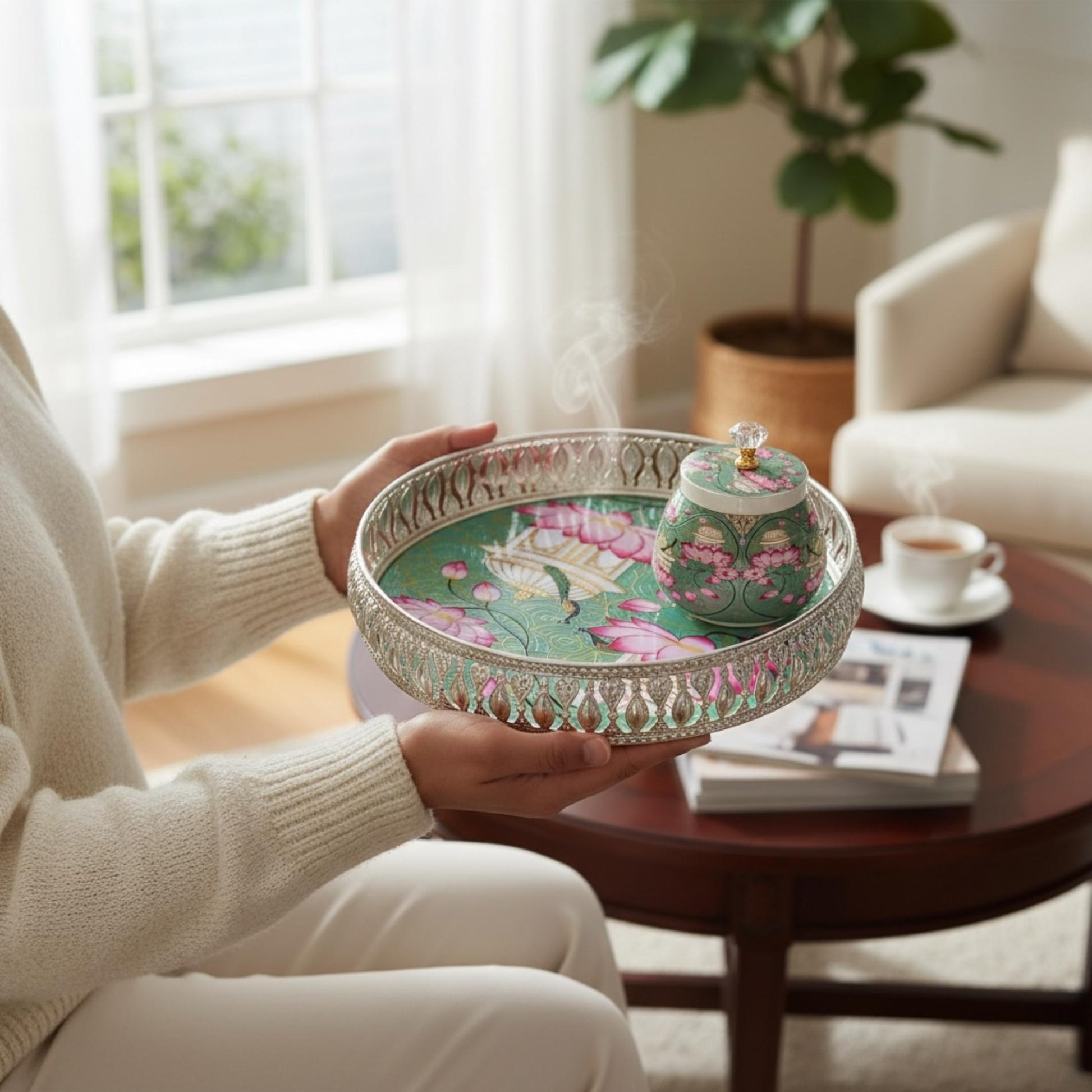 Person holding ethnic German silver Pichwai art tray in cozy living room showcasing tray size and design