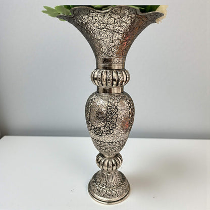 Detailed close-up of hand-engraved floral and foliage motifs on a solid brass vase with antique silver plating.