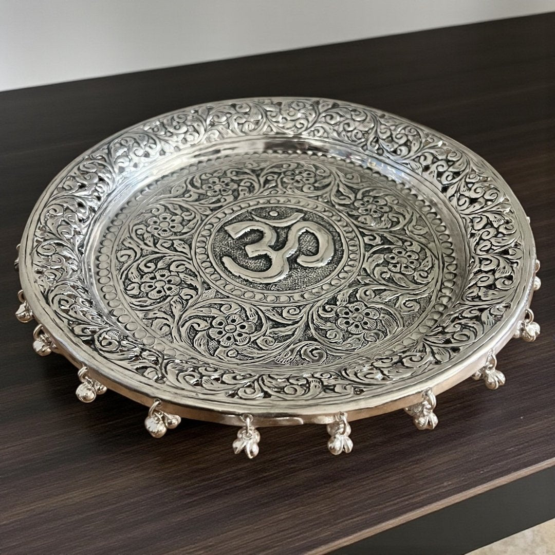 Top-down view of a 10.75-inch hand-engraved silver pooja thali with a detailed Om design and traditional floral border patterns.