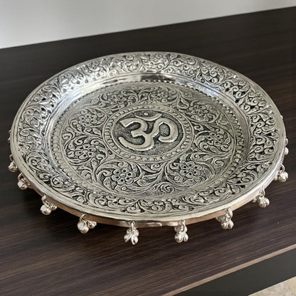 Top-down view of a 10.75-inch hand-engraved silver pooja thali with a detailed Om design and traditional floral border patterns.