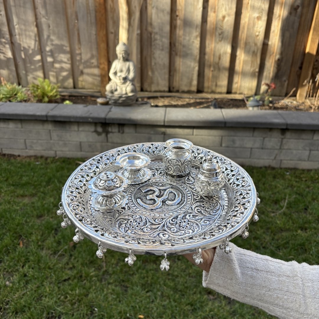 Person holding a silver pooja thali set with intricate designs outdoors