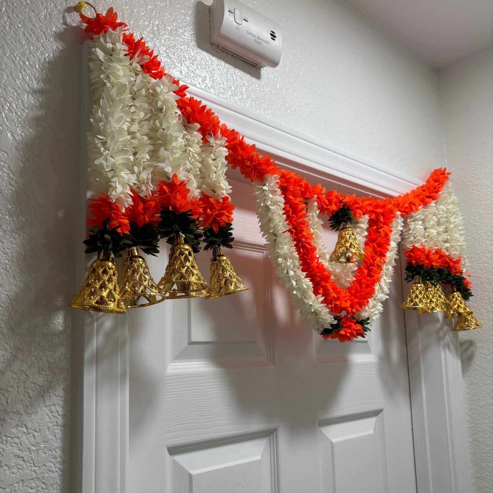 Vaibhav ivory-red marigold toran bandhanwar with gold bell on textured wall