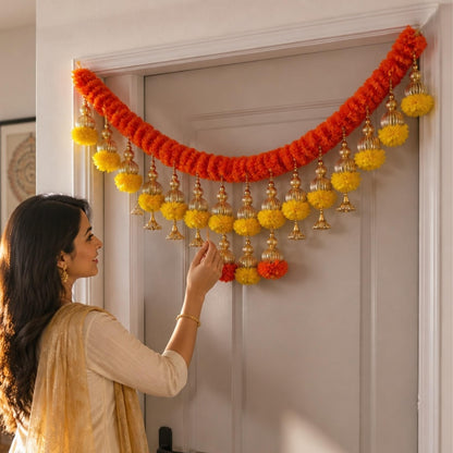Kesar orange marigold toran with yellow pompoms and gold jhumka bells on door